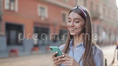 可爱的女人穿着蓝色和白色条纹连衣裙，使用智能手机上的应用程序在旧城<strong>街道</strong>上<strong>行走</strong>。 美丽美丽